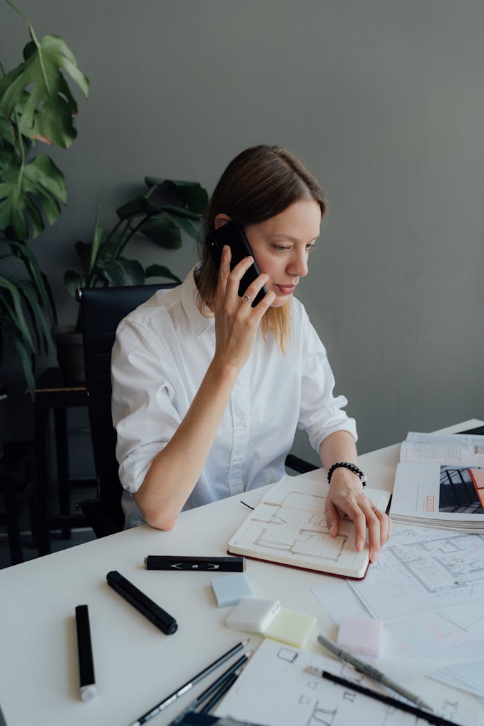 about-01 Focused woman architect discussing floor plans on the phone in an office setting.